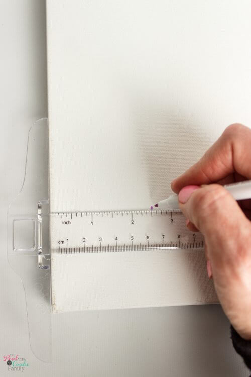 t-square on canvas showing maker marking off width of gingham Step by step tutorial on how to paint gingham and make the cutest wall art out of a craft store canvas. Perfect craft project to make DIY wall art.